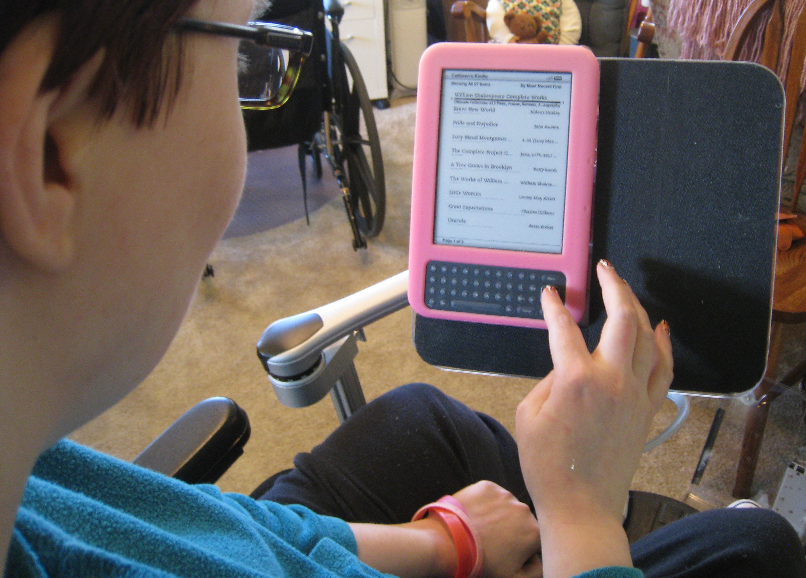 Kat uses 3 devices on her chair: a Kindle, a laptop and a speech device.